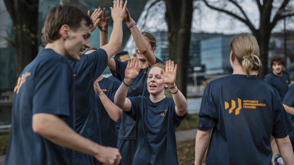 Jongeren geven elkaar high five. Op hun T-shirt staat de tekst Nationale Weerbaarheids Training. 