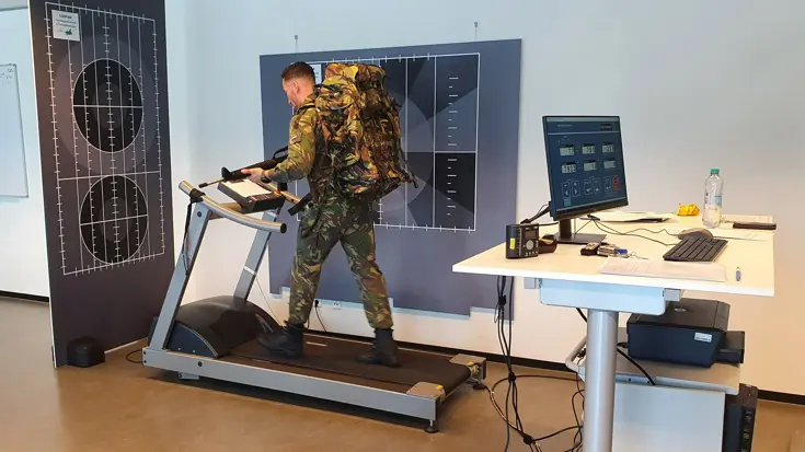 Militair loopt in een onderzoeksruimte met bepakking en nepwapen op een loopband.