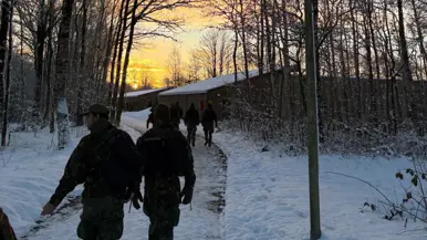Deelnemers van de Nationale Weerbaarheidstraining lopen door een besneeuwd oefengebied tijdens zonsopkomst.
