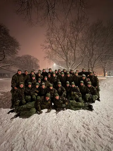 Een groep deelnemers van de Nationale Weerbaarheidstraining poseert samen in de sneeuw tijdens een avondopleiding. 