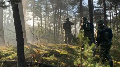 Deelnemers van de Nationale Weerbaarheidstraining lopen tijdens een veldoefening door een bosgebied.