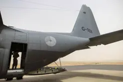 Vliegtuig van de zijkant gezien, met in de deuropening een militair.