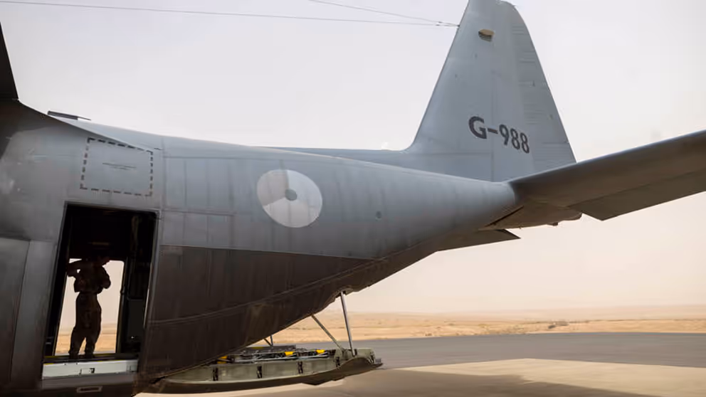 Vliegtuig van de zijkant gezien, met in de deuropening een militair.