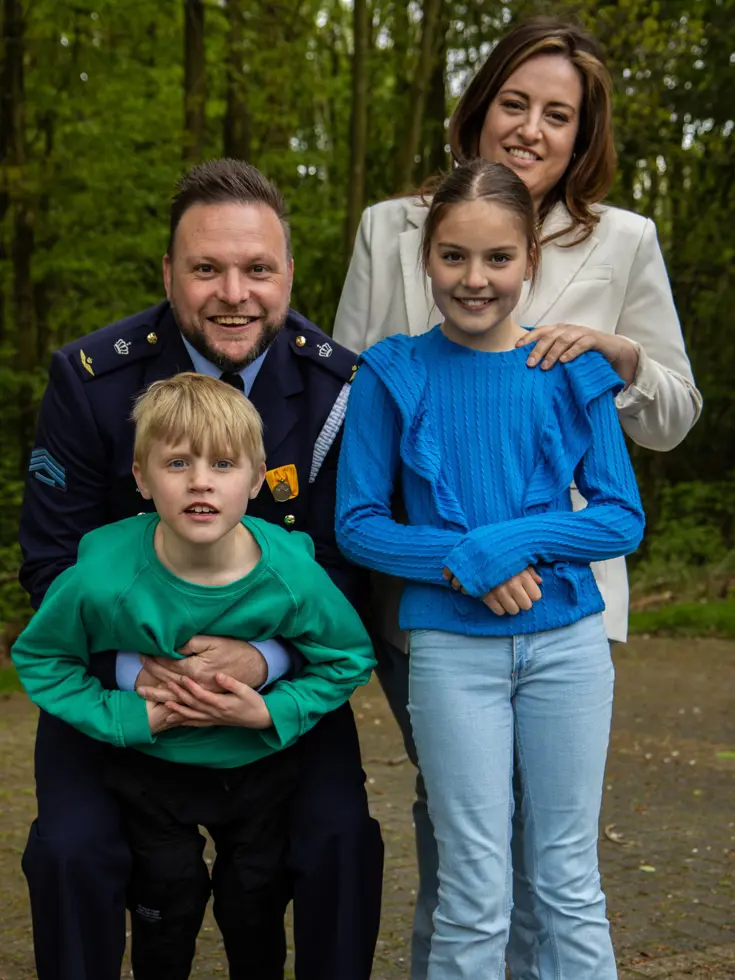 Tim poseert in zijn blauwe nette militaire pak tegen de bosrand samen met zijn vrouw, dochter en jongere zoon.