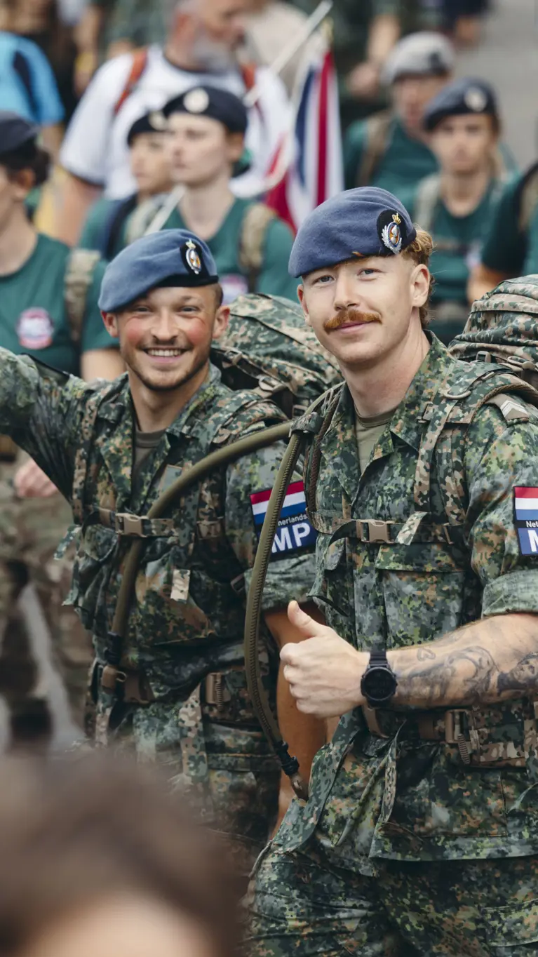 Twee militairen van de Marechaussee tijdens de 4Daagse, in groen tenue, steken hun duim op naar de camera.