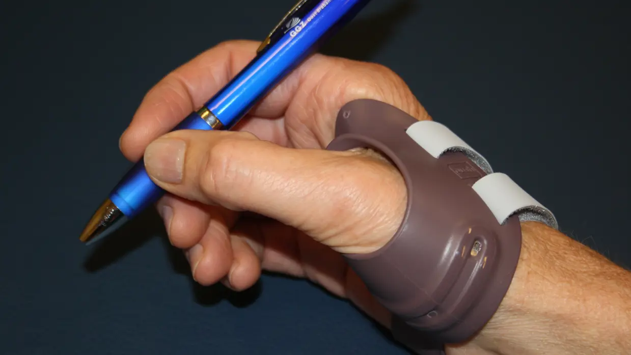 Een hand met een een kunstspalk houdt een pen vast.
