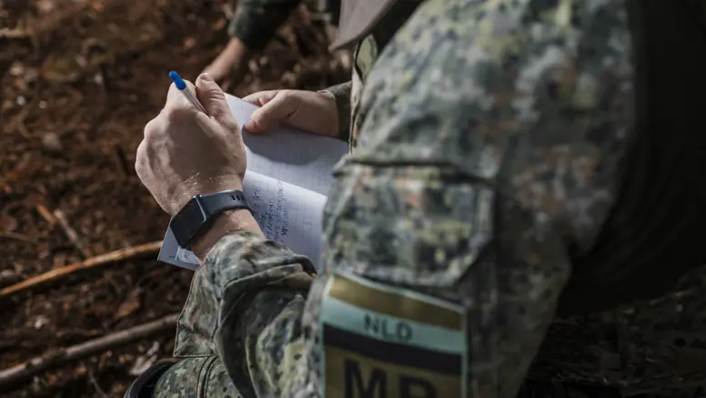 Een marechaussee van het MP-eskadron in groen tenue met een notitieblok en pen in zijn hand.