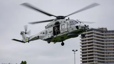 Een Chinook stijgt op boven een veld, met aan een lange kabel de Nederlandse vlag
