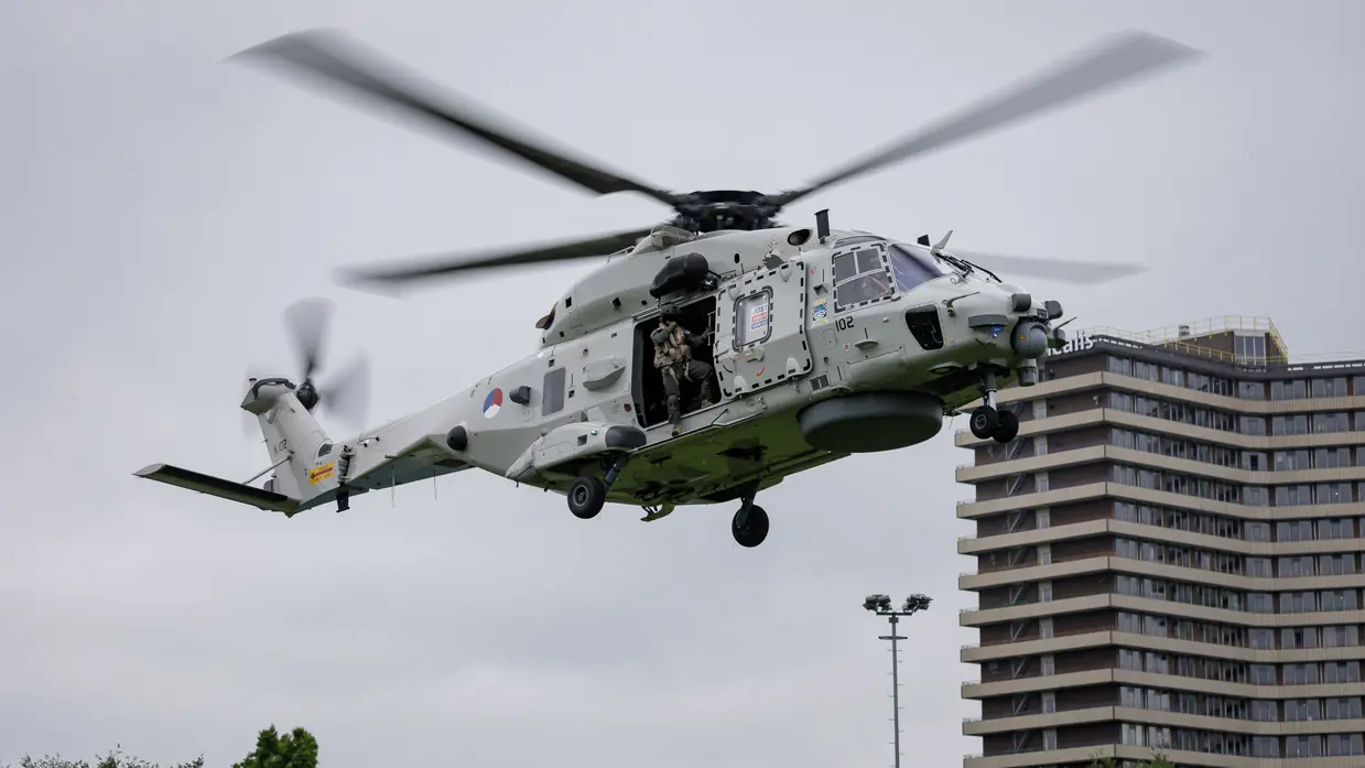 Een Chinook stijgt op boven een veld, met aan een lange kabel de Nederlandse vlag