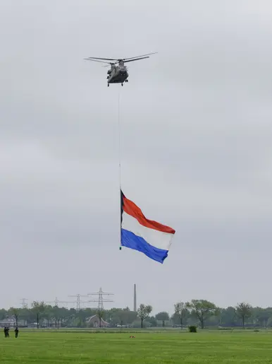 Een Chinook stijgt op boven een veld, met aan een lange kabel de Nederlandse vlag