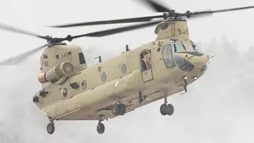 Een helikopter maakt een landing op een wit veld. Rechts met een paar pakketten onder zich. 