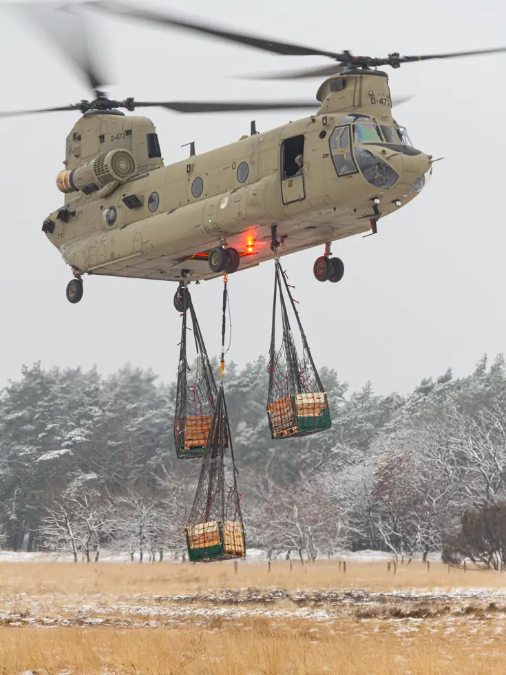 Een helikopter maakt een landing op een wit veld. Rechts met een paar pakketten onder zich. 