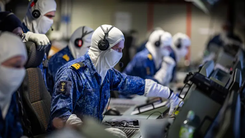 Marinepersoneel zit in een ruimte vol computers. Ze dragen witte bivakmutsen.