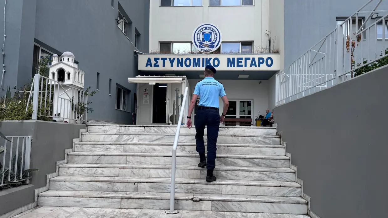 Een marechaussee, op de rug gezien, loopt de trap op naar de ingang van een Griek politiebureau.