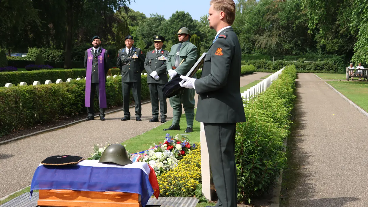 Militairen brengen de laatste groet bij een kist met een vlag en een helm erop.