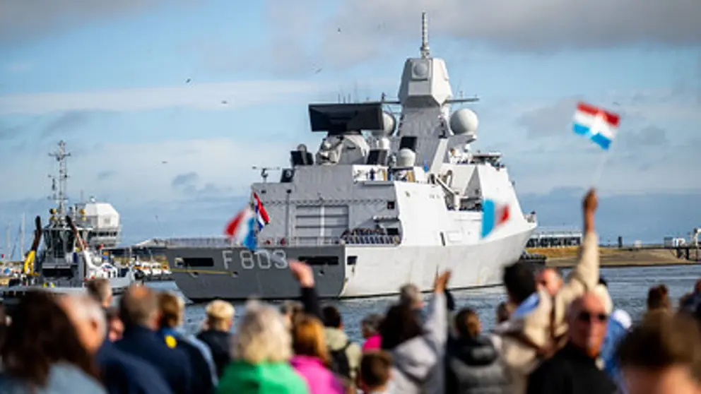 Familie en vrienden zwaaien vanaf kade enthousiast naar marineschip dat terugkeert van missie.