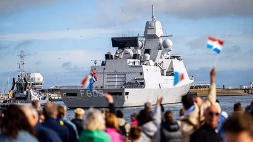 Familie en vrienden zwaaien vanaf kade enthousiast naar marineschip dat terugkeert van missie.