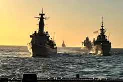 Marineschepen varen achter elkaar op zee.