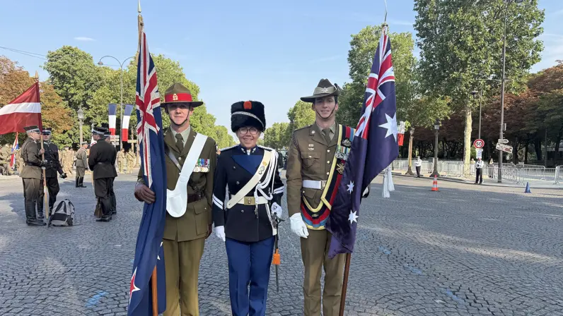 Kim staat in ceremonieel tenue tussen twee buitenlandse collega’s. Zij houden allebei een vlag vast.