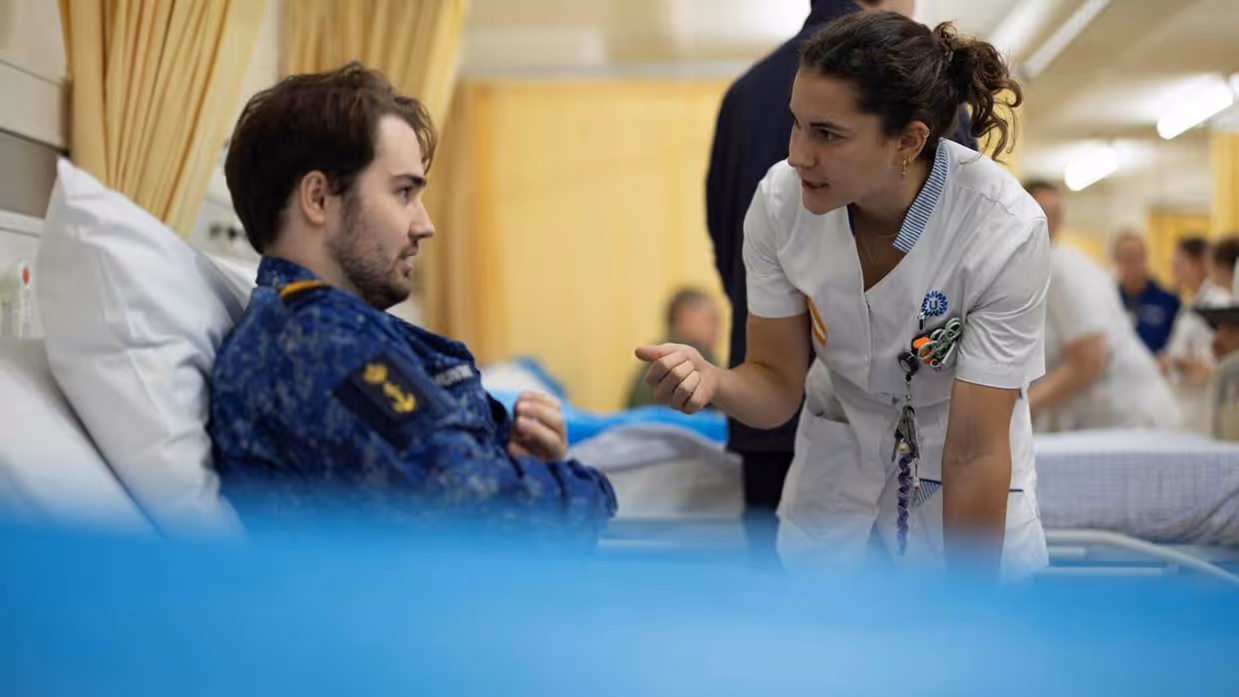 Militair in ziekenhuis bed. Verpleegster praat met hem.