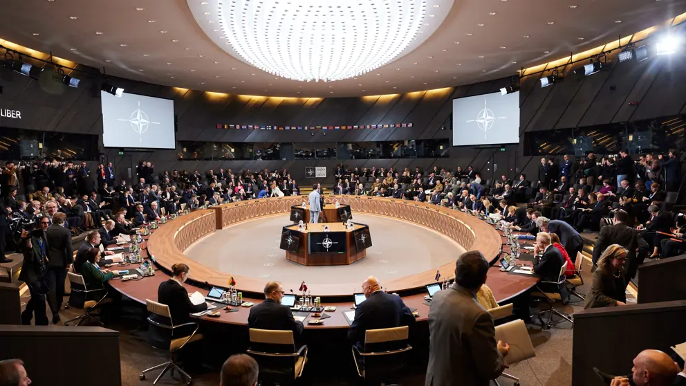 Defensieministers van de NAVO vergaderen aan een cirkelvormige tafel.