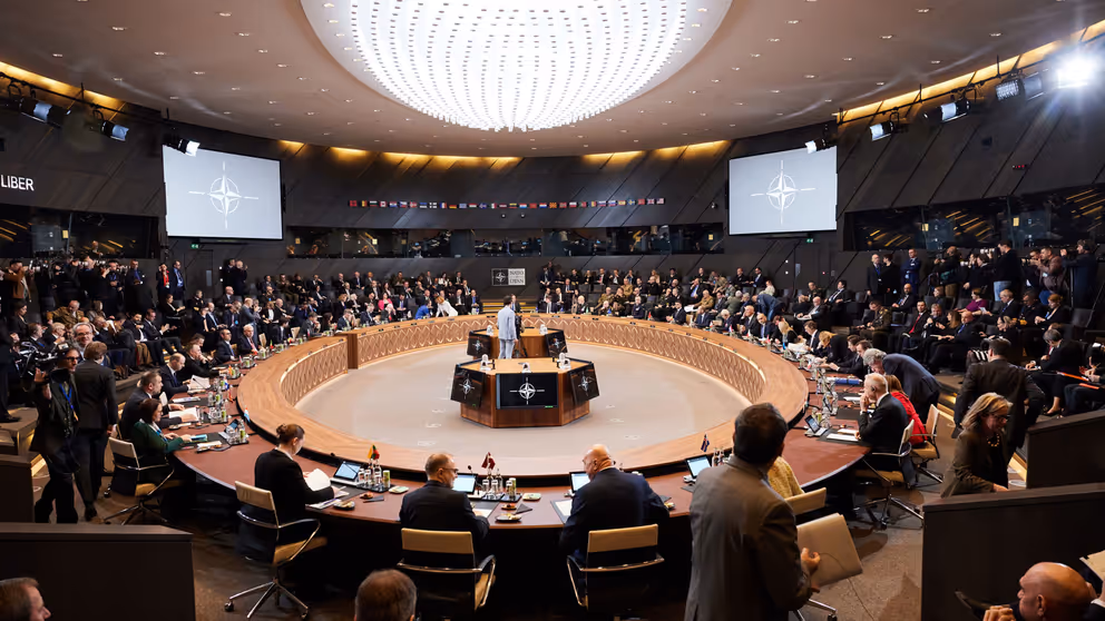 Defensieministers van de NAVO vergaderen aan een cirkelvormige tafel.