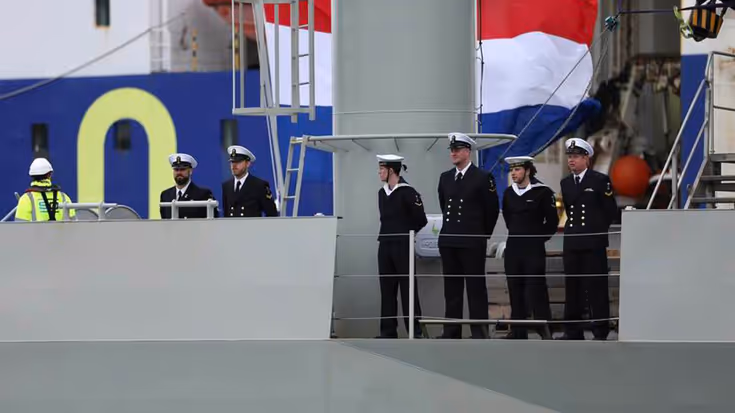 Bemanning staat op het dek. Op de achtergrond de Nederlandse driekleur.