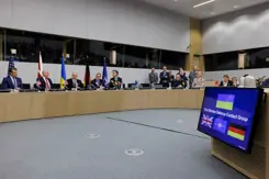 Zaal met sprekers van de 31e Ukrain Defence Contact Group. Op de voorgrond is veel grijze vloer zichtbaar.