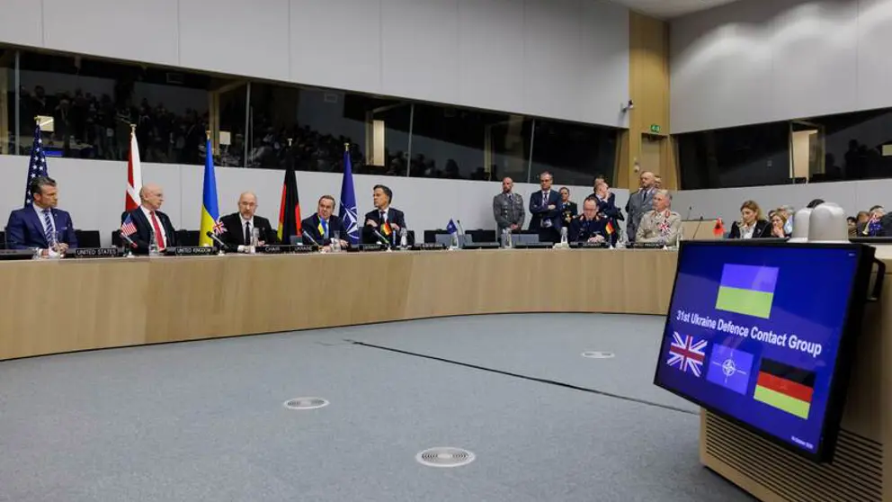 Zaal met sprekers van de 31e Ukrain Defence Contact Group. Op de voorgrond is veel grijze vloer zichtbaar.