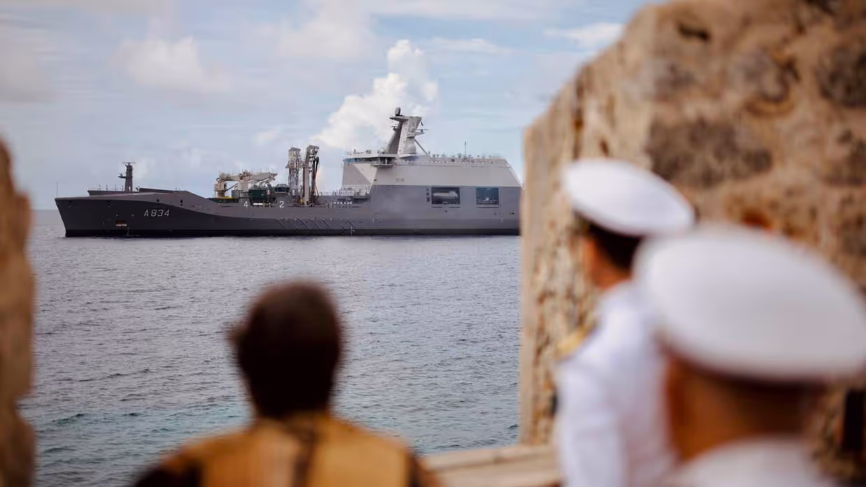 Marineschip geeft saluutschoten af, mensen kijken ernaar.