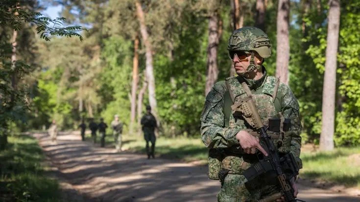 Marechaussee in groen uniform, met een lang wapen in de hand.