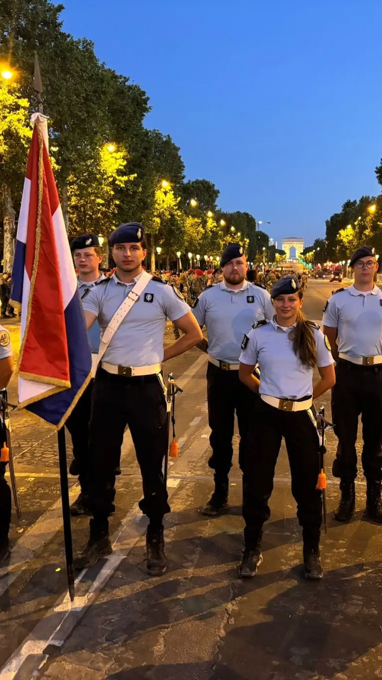 Een groep marechaussees staat in het lantaarnlicht in Parijs. Een persoon houdt de Nederlandse vlag vast.
