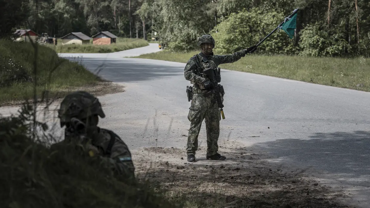 Marechaussee in groen tenue met een groene vlag in zijn hand met op de voorgrond een andere militair.