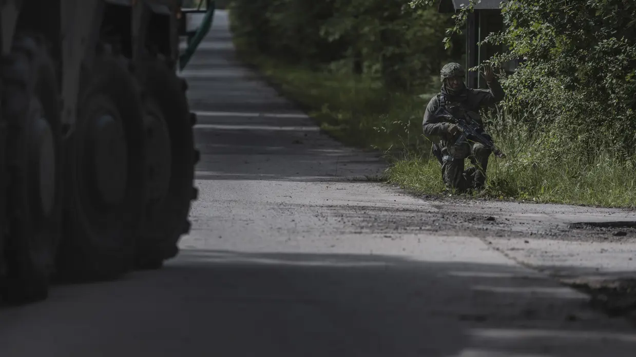 Militair in groen tenue aan de kant van de weg met zijn hand omhoog.