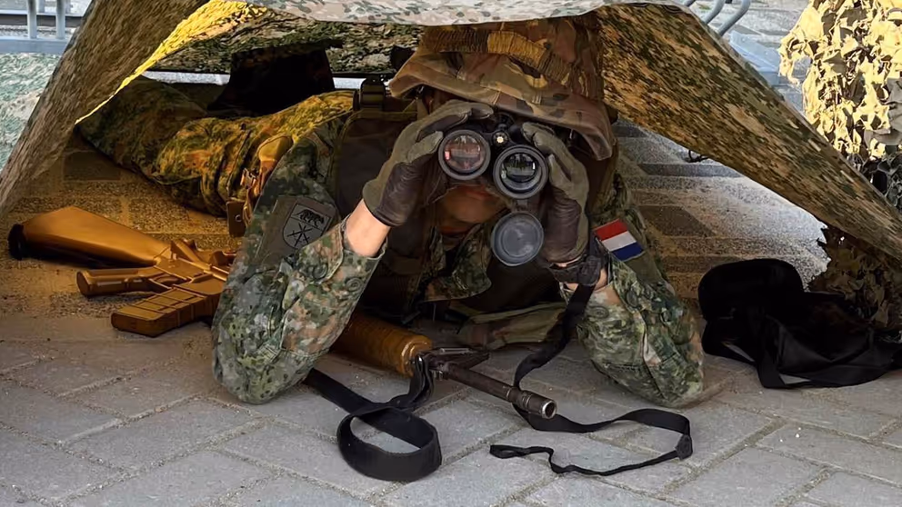 Militair met verrekijker onder tentdoek.