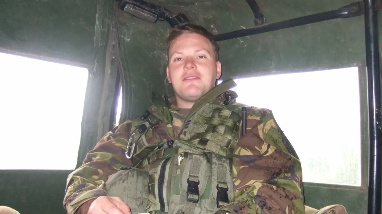 Een jonge Tim Nelissen in gevechtstenue zittend achterin in een militair voertuig. Hij kijkt in de camera.