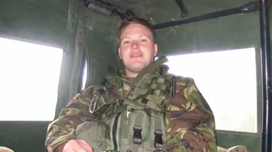 Een jonge Tim Nelissen in gevechtstenue zittend achterin in een militair voertuig. Hij kijkt in de camera.