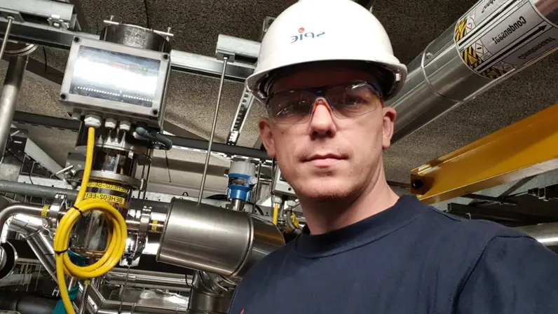 Glenn Afman met een witte helm en veiligheidsbril op vlak naast het binnenwerk van een machine.