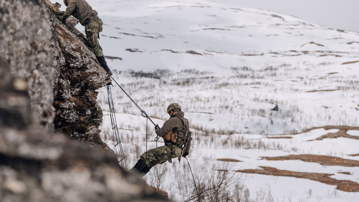 Twee militairen die een rots beklimmen in een sneeuwachtig gebied