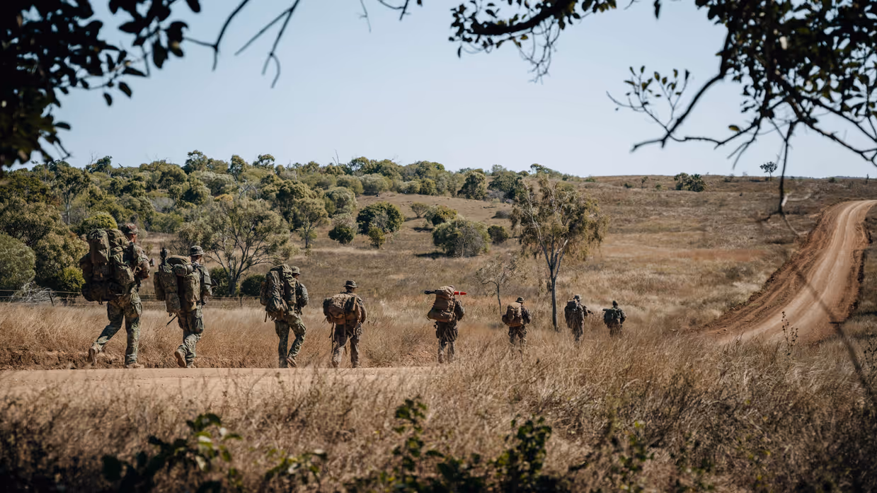 Militairen marcheren op een weg in Australisch landschap.