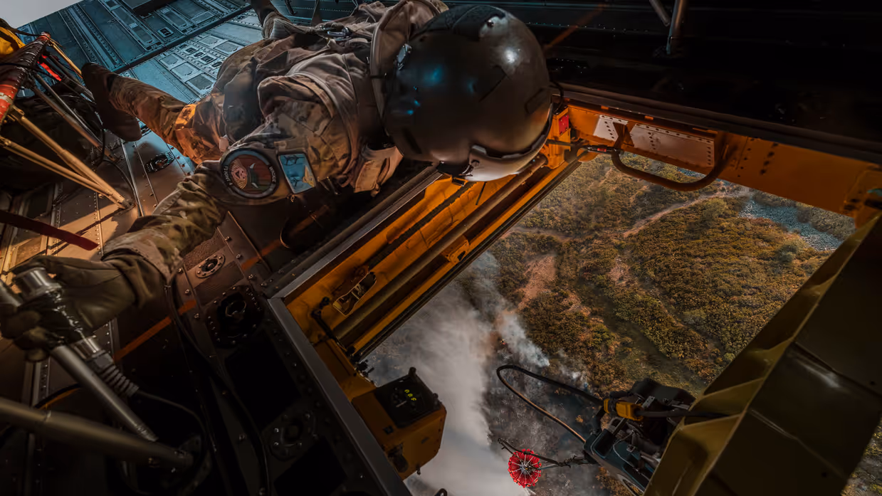 Militair kijkt vanuit een helikopter naar een bosbrand beneden