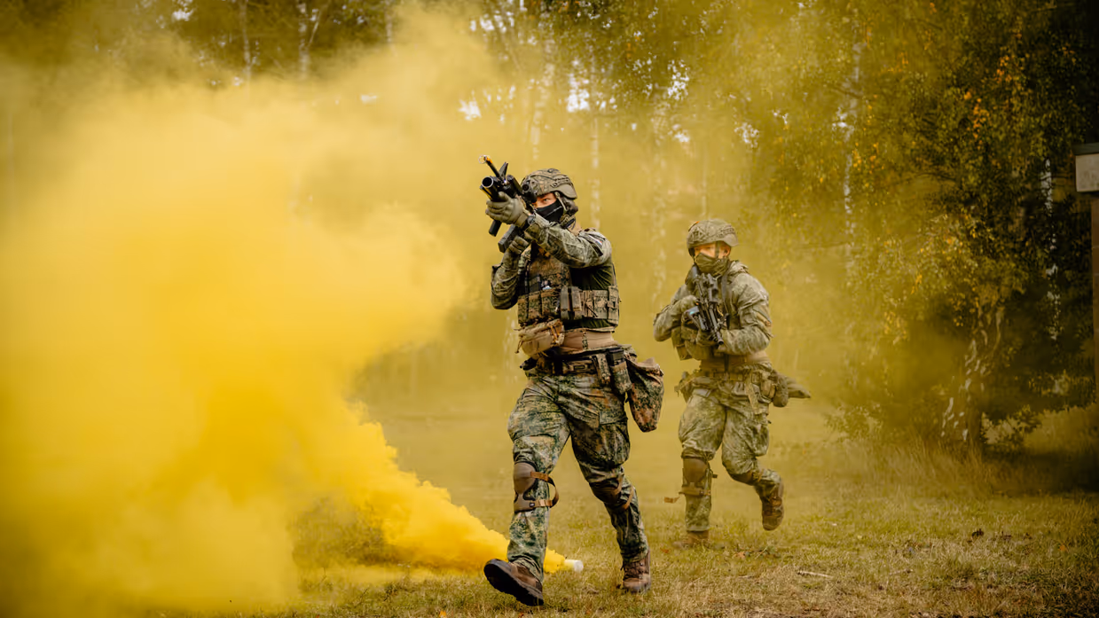 Twee militairen lopen met wapens door een rookgordijn.
