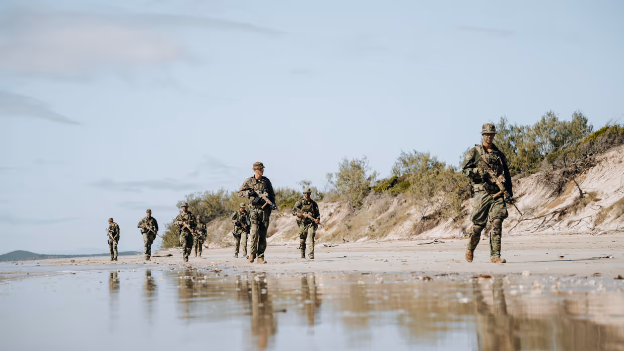Militairen lopen langs water in Australisch landschap.