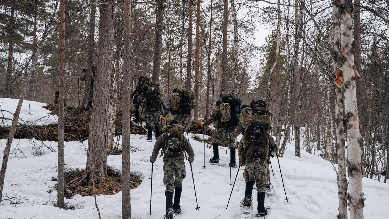 Een groep militairen wandelt door een besneeuwd bos met volle bepakking