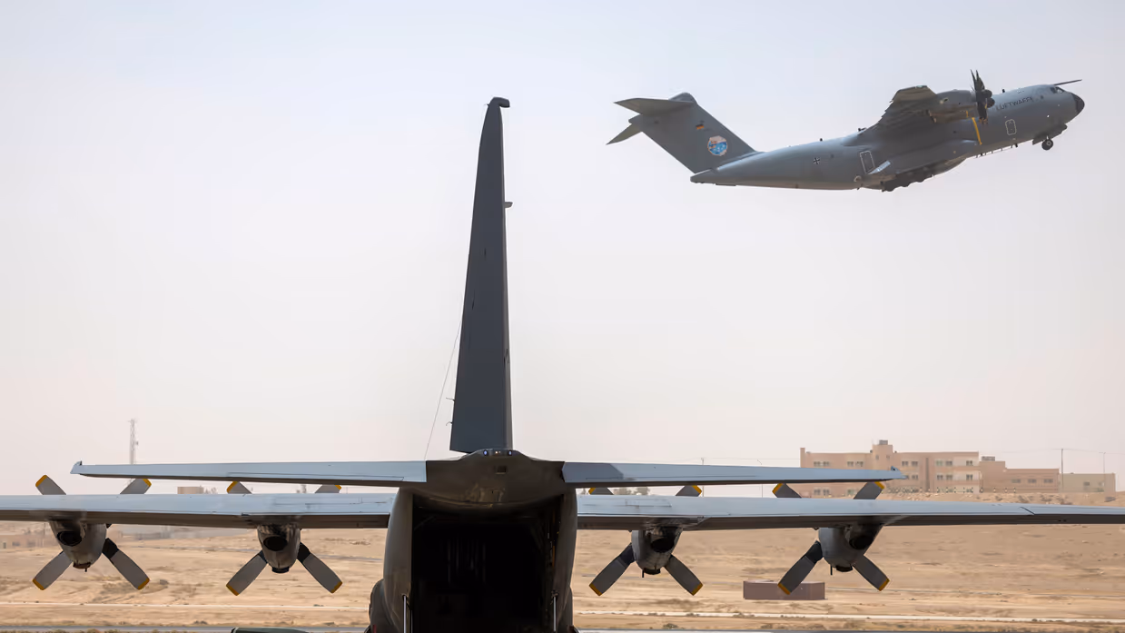 Een C-130 transportvliegtuig dat klaarstaat en een transportvliegtuig die opstijgt in de achtergrond..