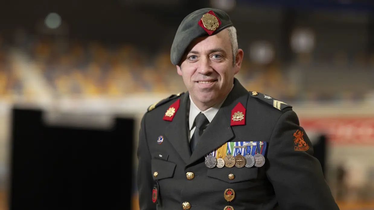 Militair met baret op en borst vol medailles kijkt lachend in camera. 