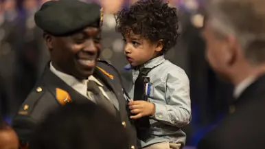 Kinderen van militair krijgen kindermedaille uitgereikt. Militair in uniform kijkt lachend in camera. 