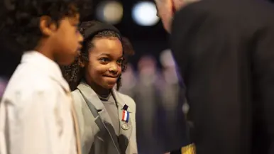 Kinderen van militair krijgen kindermedaille uitgereikt. Militair in uniform kijkt lachend in camera. 