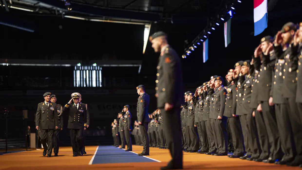 Parade-inspecteur loopt langs militairen tijdens medaille-uitreiking in sporthal.
