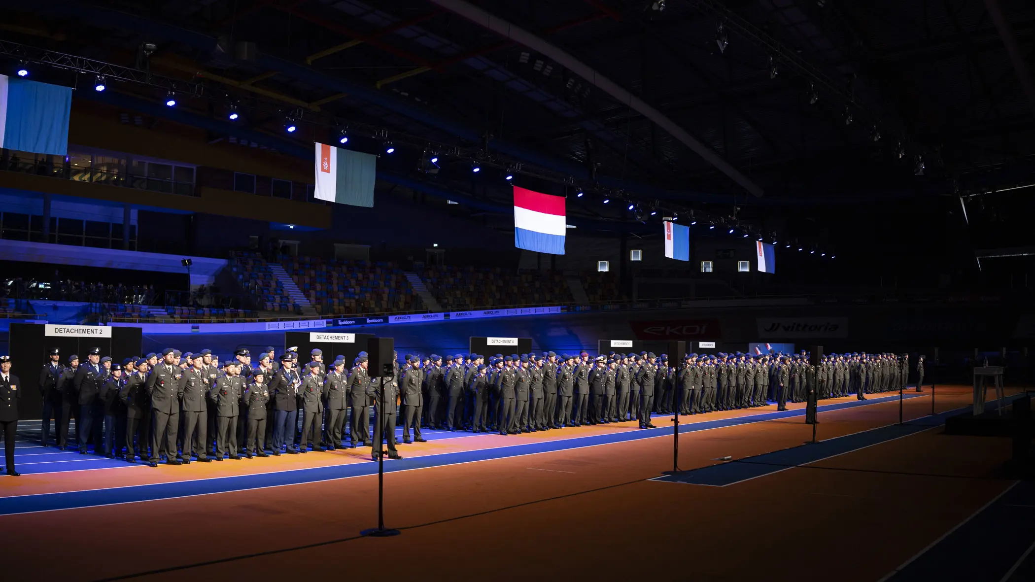 Militairen in dagelijks tenue staan naast elkaar opgesteld in een grote hal tijdens medaille-uitreiking.